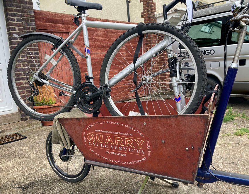 The trailer on the front of a cargo bike loaded with a bike being taken for repair by a mobile cycle repair company