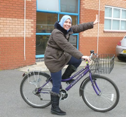 Woman cyclist wearing headscarf and waving having been given Sanctuary Wheels bike