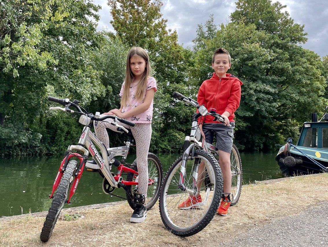 Girl and boy posing on bikes on river bank