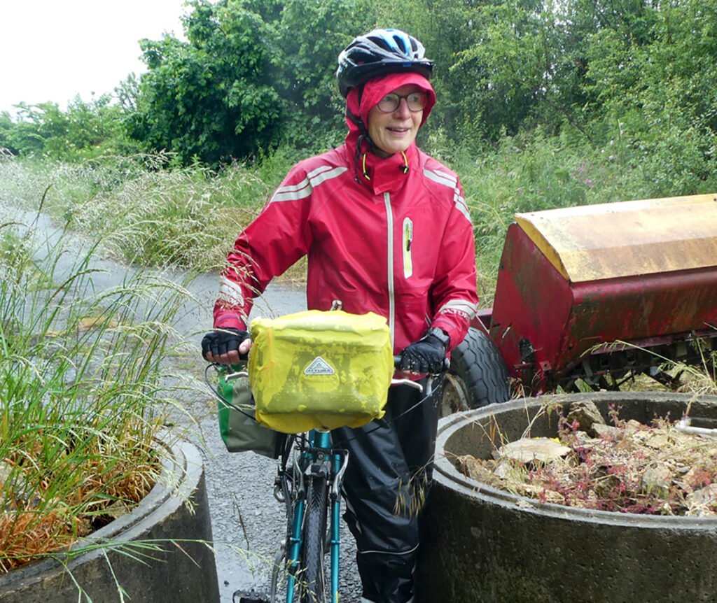 Cyclist in red waterproof with hood up and helmet over the hood