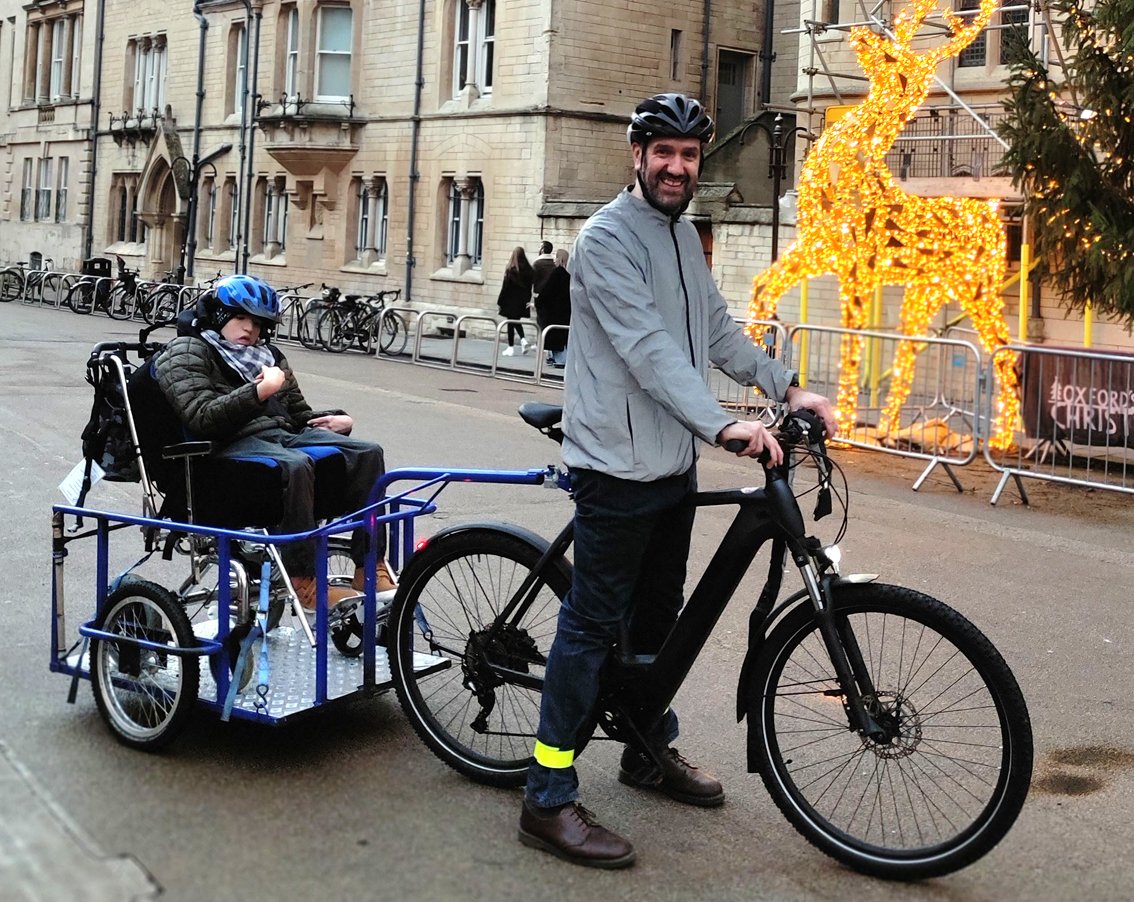 Boy in wheelchair on trailer towed by cargo bike, Broad Street Oxford