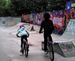 Child being taught to ride two-wheel bike in a skate park