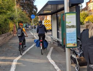 Two cyclists on cycle path pass close to bus shelter in Woodstock Road