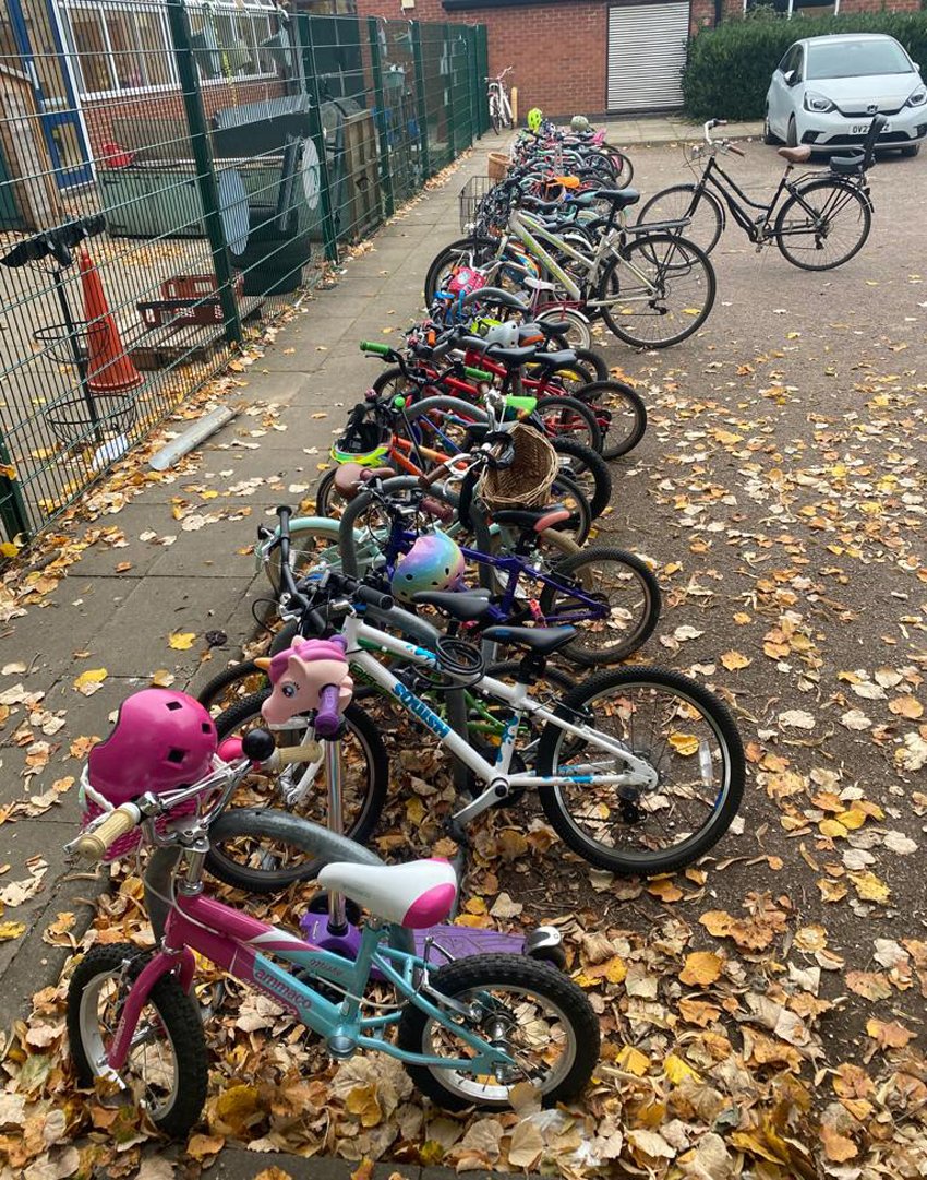 Cycle rack in school filled with kids' bikes, one parked car in background, authumn leaves on ground
