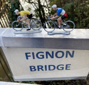 Sign saying 'Fignon Bridge' with two tiny models of cyclists on top