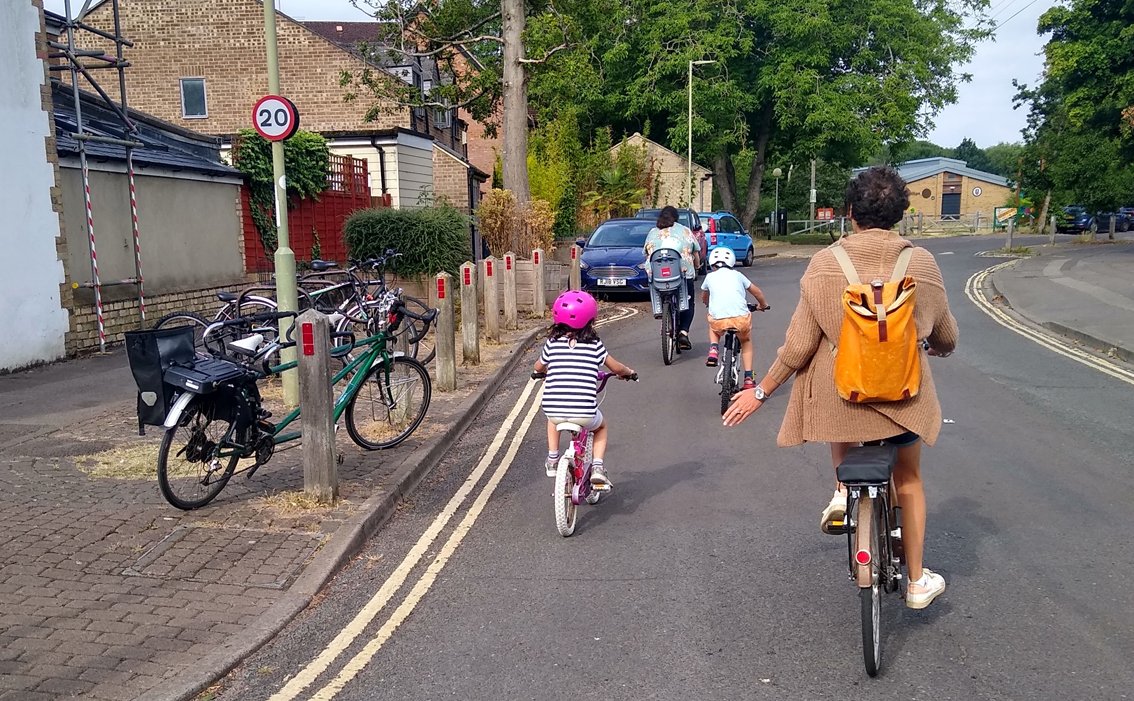 Back view of two adults and two primary-age children cycling to St Ebbes School in Oxford in a road without other traffic.